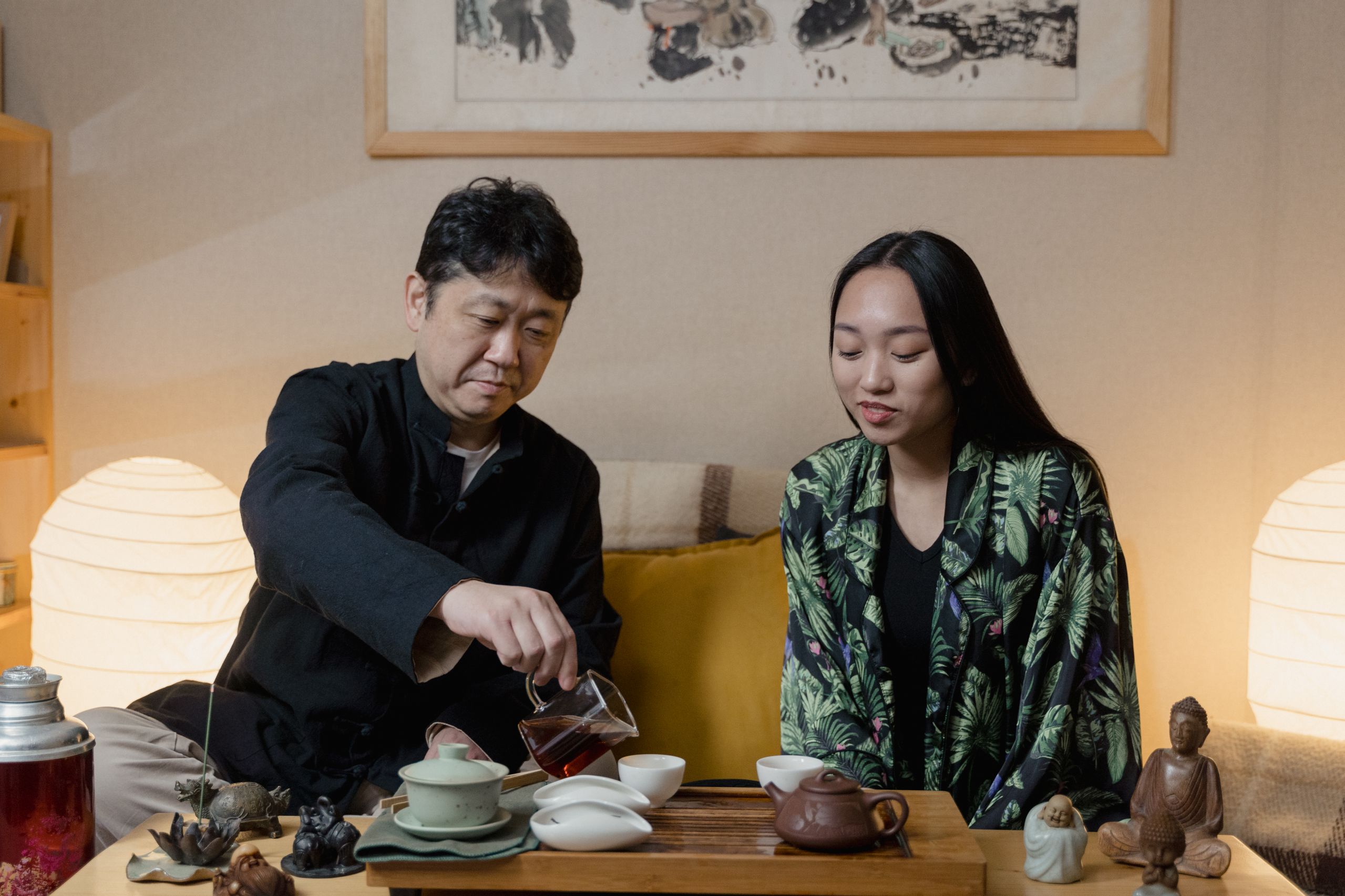 Man and woman smiling and pouring tea at a wooden table inside a tea shop